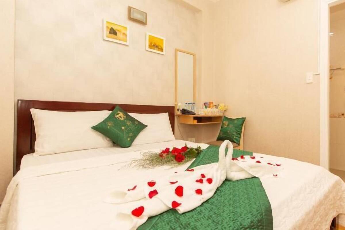 A hotel room with a bed, a bedside table with a mirror, a green pillow, and a bouquet of flowers.