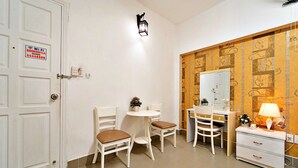 A room with a white door, a Wi-Fi sign, a small table with chairs, a desk with a lamp, and a dresser. - S79 Bao Khoi Hotel (Ho Chi Minh City)