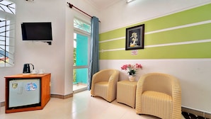 A room with a TV, a small wooden desk, two wicker chairs, a framed picture, and a potted plant. - S79 Bao Khoi Hotel (Ho Chi Minh City)