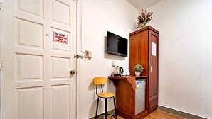 A room with a white door, a wooden cabinet with a TV mounted above it, a small stool, and a plant on top of the cabinet. - S79 Bao Khoi Hotel (Ho Chi Minh City)