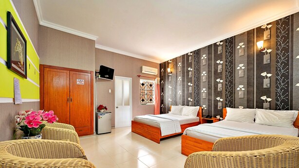 A hotel room with two beds, wicker furniture, a small kitchenette, and a decorative wall with a floral pattern. - S79 Bao Khoi Hotel (Ho Chi Minh City)