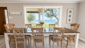 Uma sala de jantar com uma mesa grande e seis cadeiras, vista para o exterior e uma porta com cabideiro.