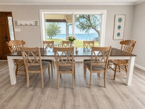 A dining area with a large table and six chairs, a view of the outdoors, and a door with a coat rack.