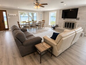 A living room with a sofa, a coffee table, a fireplace, a TV, and a dining area with chairs and a table.
