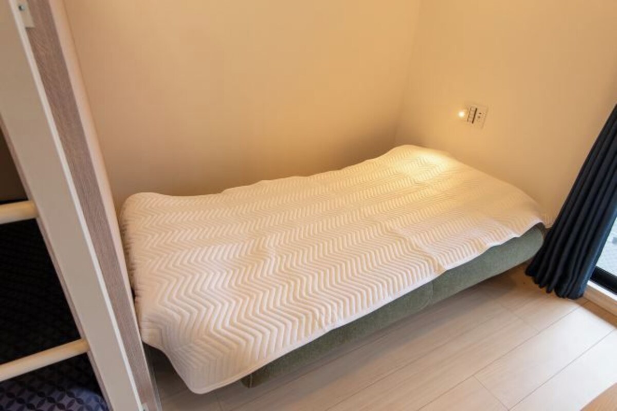 A small, single-bed room with a simple, clean design, featuring a bed with a patterned bedspread and a plain wall.