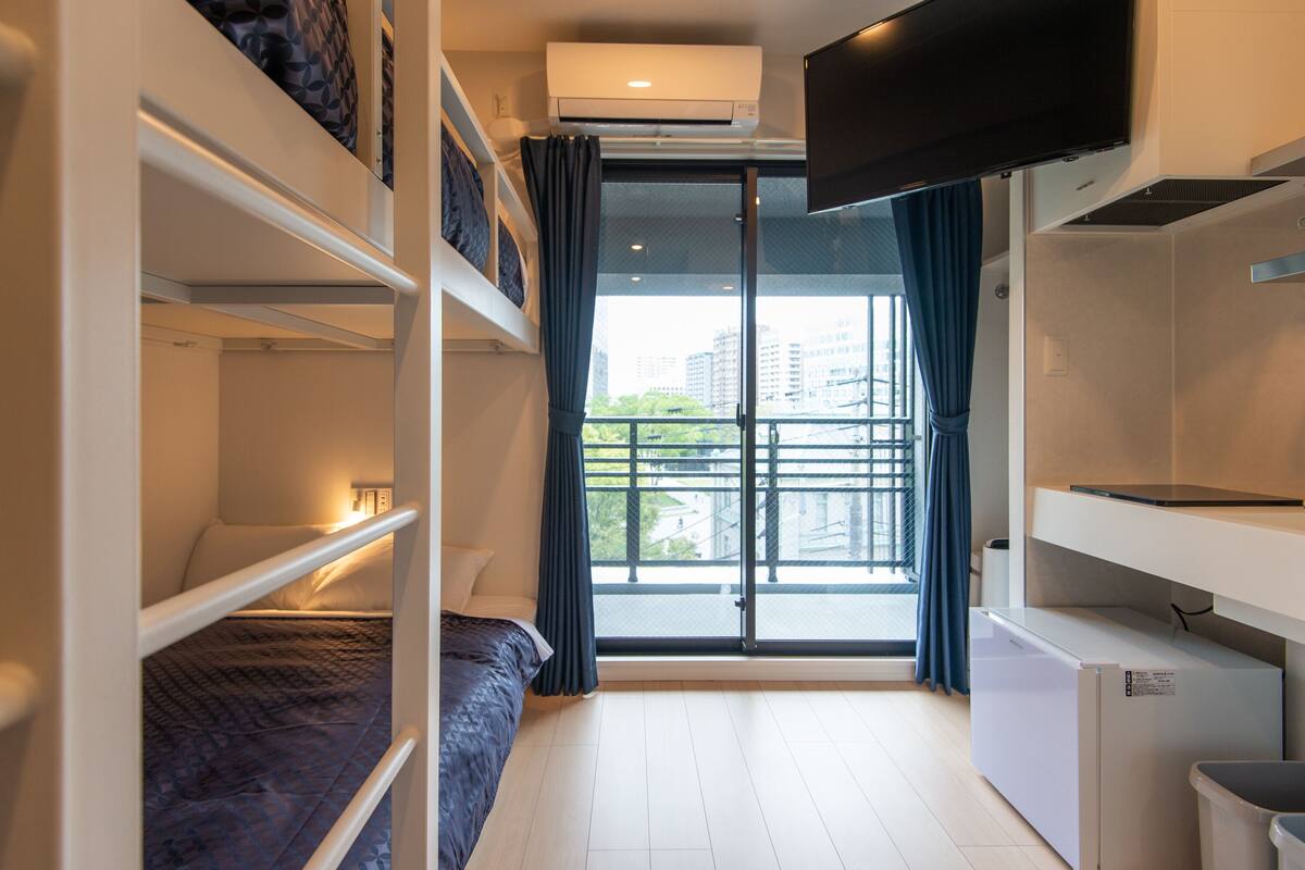 A compact hotel room with bunk beds, a flat-screen TV, a mini-fridge, and a balcony with a city view.