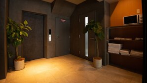 Un pasillo con dos plantas en macetas, una puerta con un cartel y un estante con toallas dobladas.