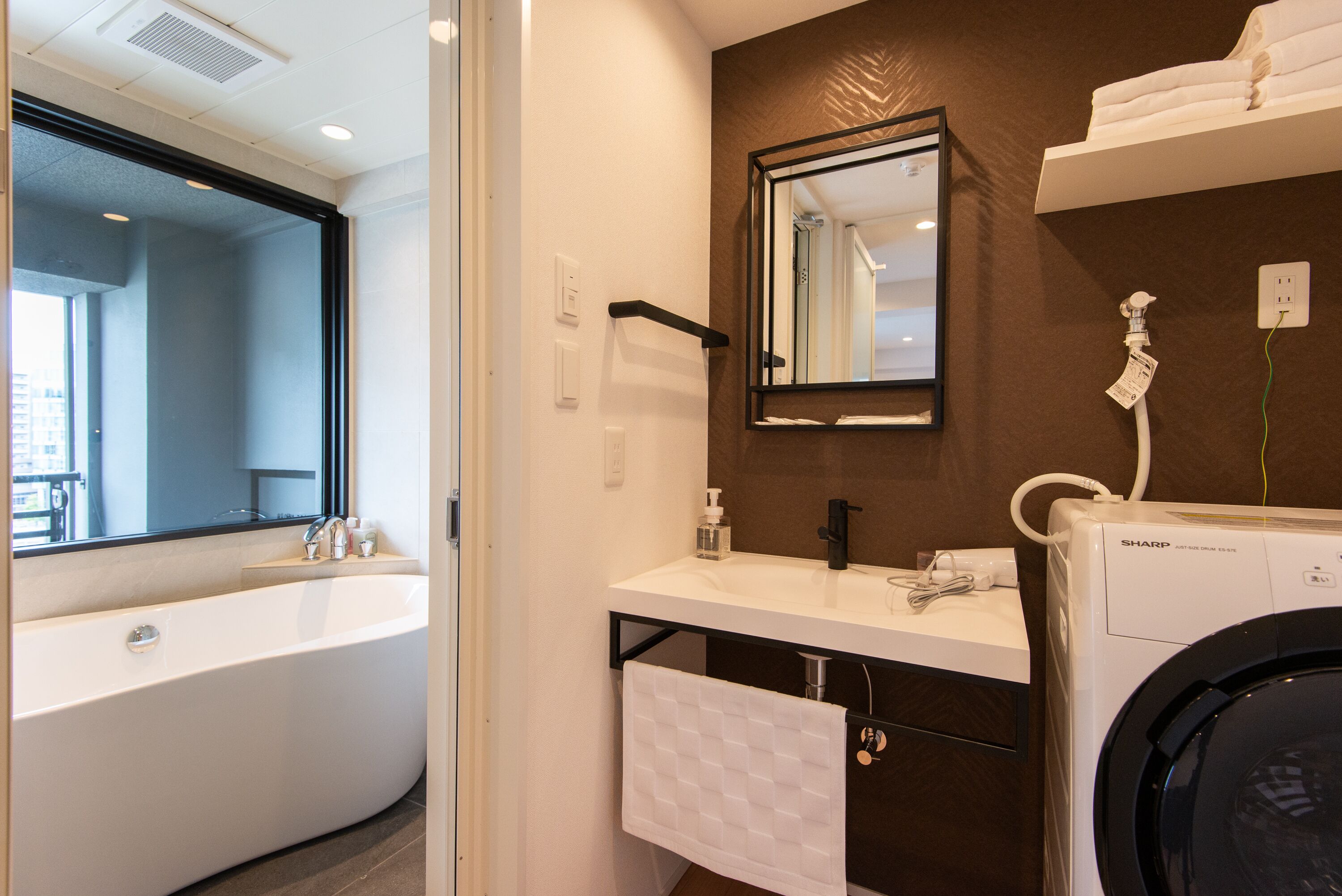 A modern bathroom with a bathtub, a sink, a mirror, and a washing machine.