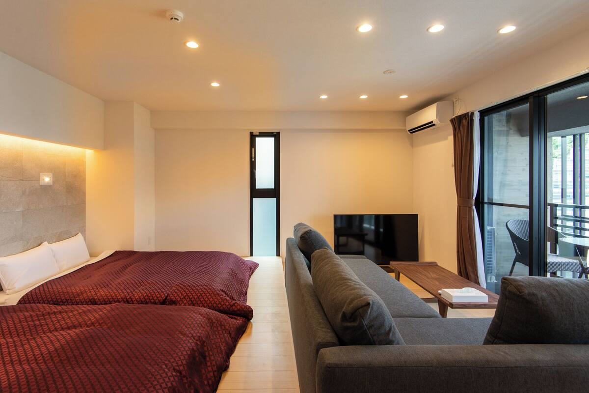 A modern hotel room with two beds, a sofa, a TV, and a large window.