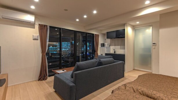 Una habitación de hotel moderna con sofá, cama, televisión y vistas a la ciudad desde la ventana.