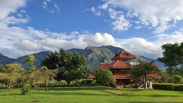A traditional building with a red roof, surrounded by a well-maintained park with trees and a clear view of mountains in the background. - Avadale Masinagudi - Stag Groups Not Allowed  (Ootacamund)