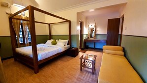 A four-poster bed with a wooden frame, a small wooden table, a sofa, and a mirror in a room with green and white walls. - Avadale Masinagudi - Stag Groups Not Allowed  (Ootacamund)