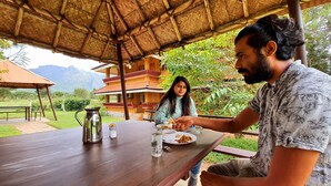 A wooden table with a metal pitcher and a glass of water, set outdoors under a thatched roof. - Avadale Masinagudi - Stag Groups Not Allowed  (Ootacamund)