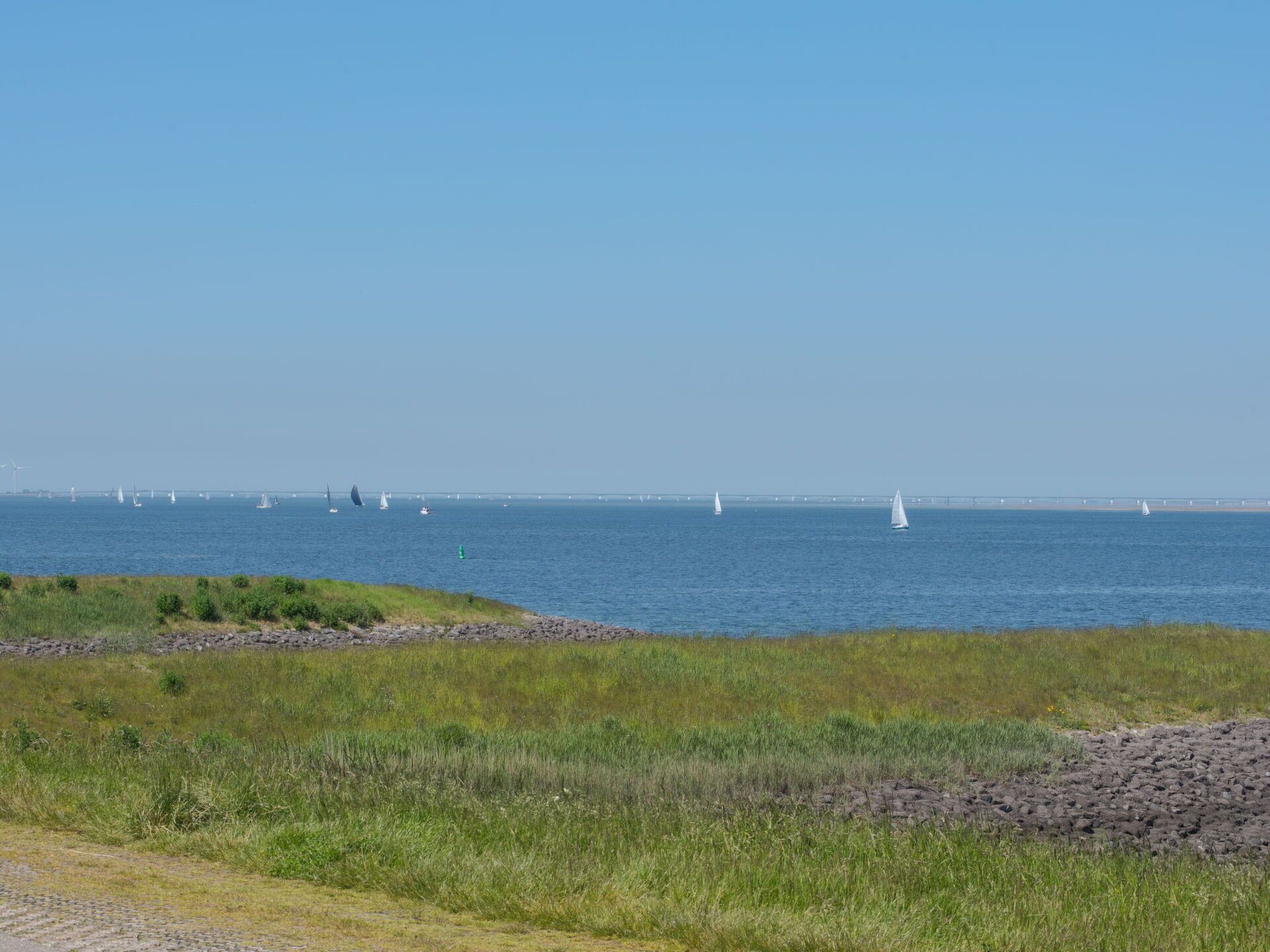 A coastal landscape with a clear sky, a body of water, and a distant bridge.