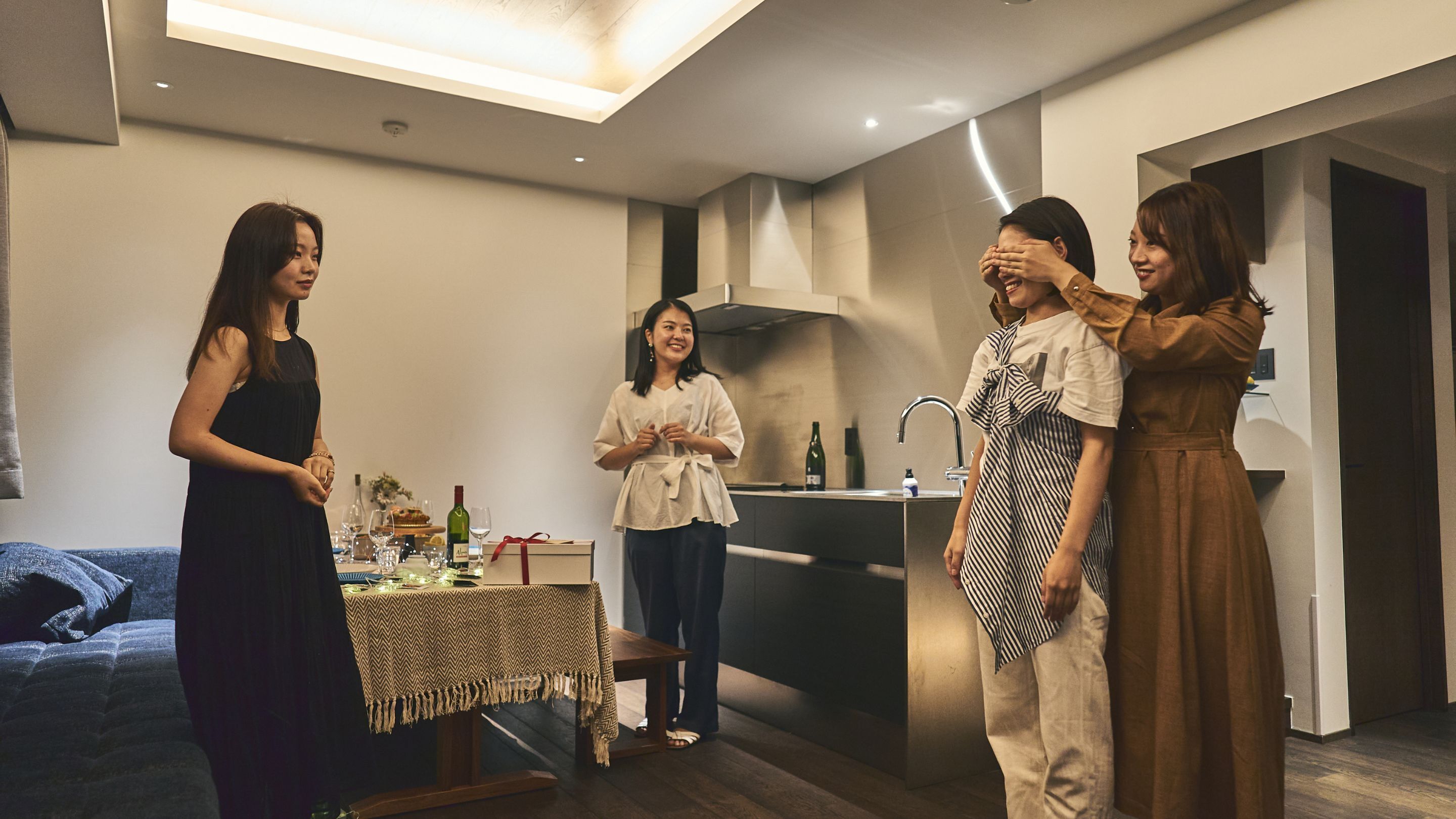 Uma sala moderna com uma mesa de jantar posta para uma refeição, área de cozinha com pia e fogão, e uma cama ao fundo.