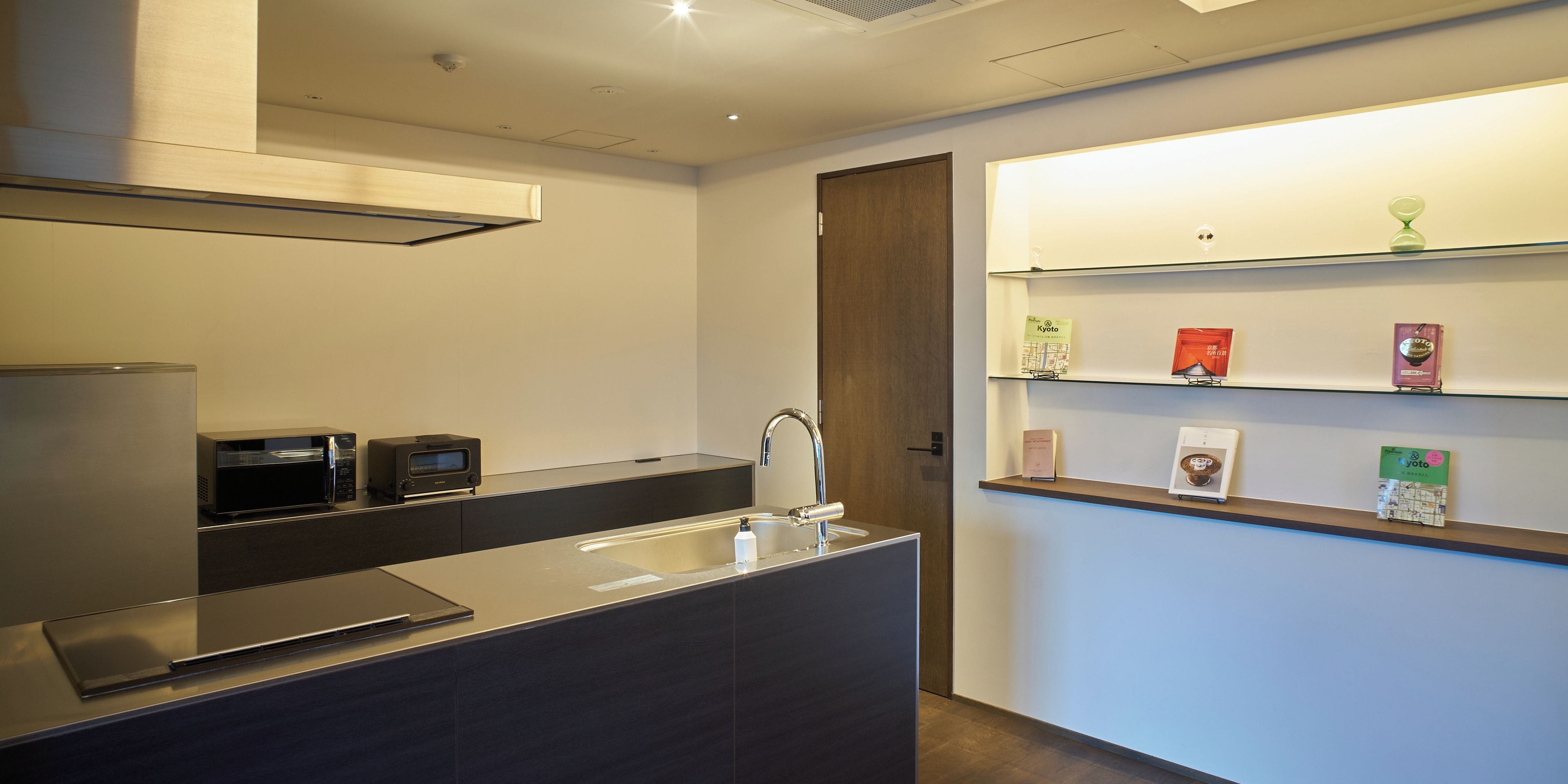 A modern kitchen with a built-in microwave, toaster, and sink. There are books and a clock on the wall.