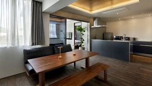A modern living room with a wooden dining table, a black leather sofa, and a kitchen area with a built-in island. - 20 Pieces (Kyoto)