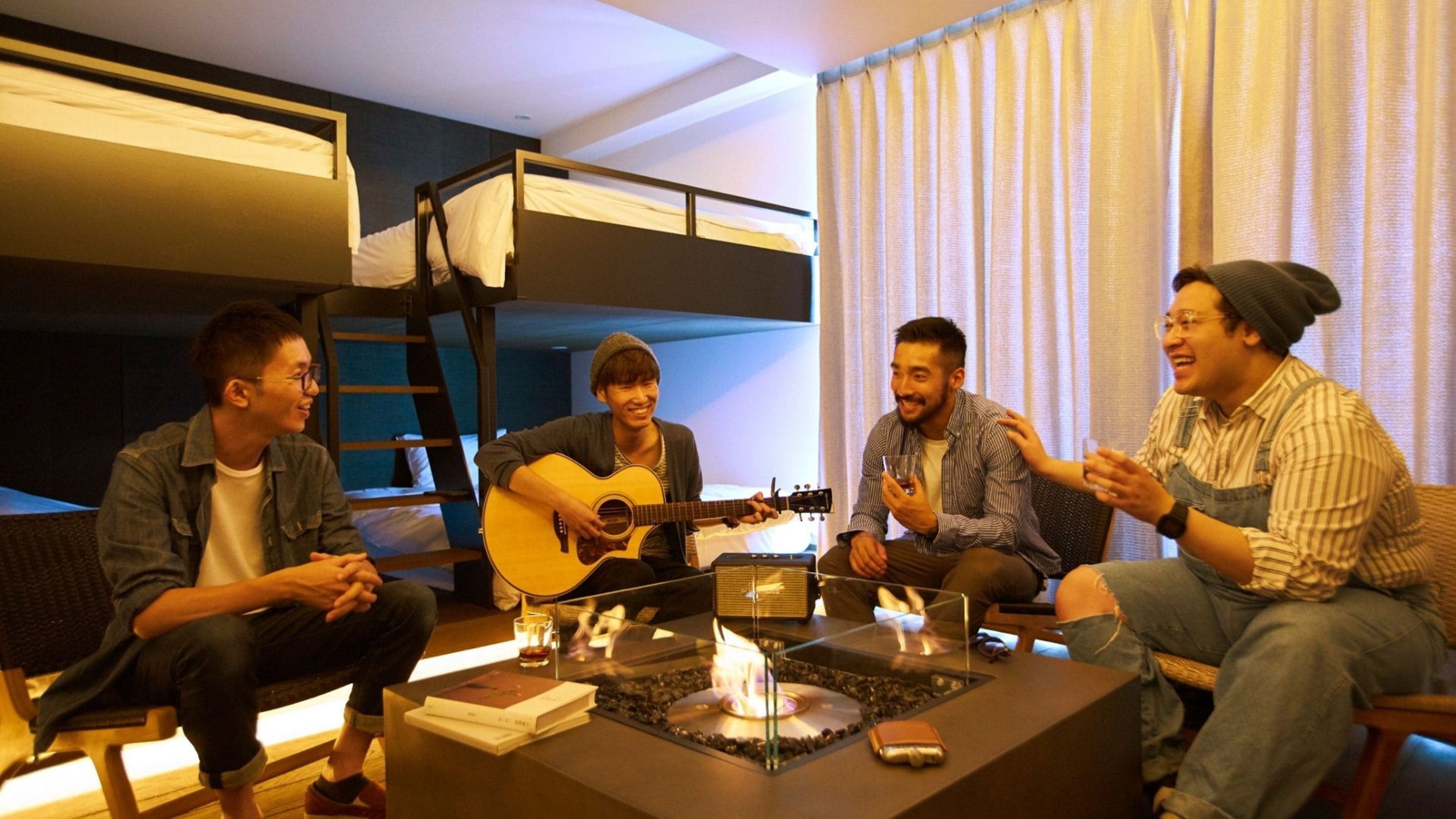 A group of people sitting around a table with a guitar and a small fire.