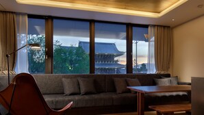 A modern living room with a sofa, a wooden coffee table, and a floor lamp. Large windows offer a view of traditional architecture. - 20 Pieces (Kyoto)