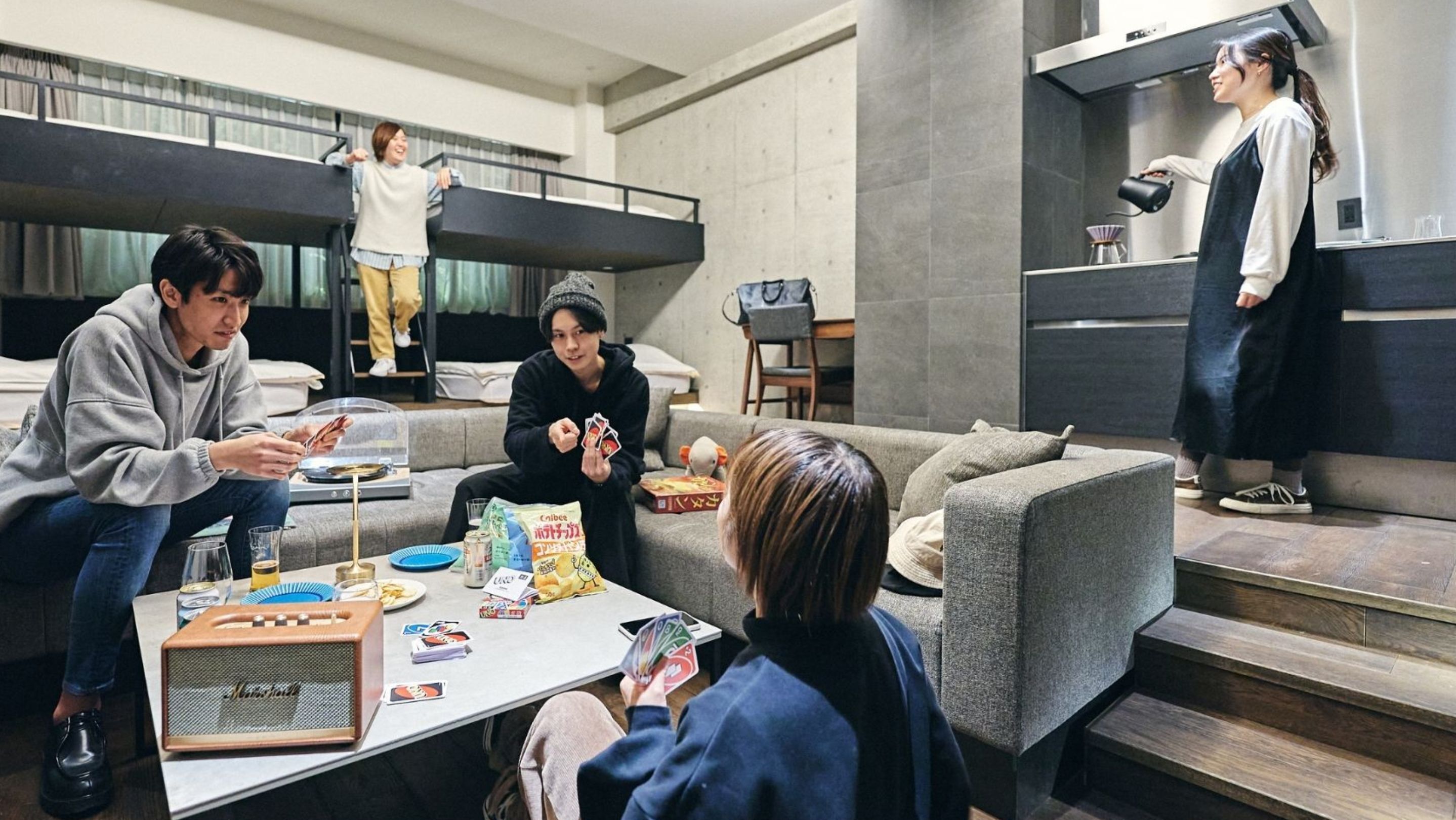 A modern living room with a sofa, a coffee table with snacks, and a person playing cards.