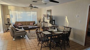 A living room with a sofa, coffee table, dining table, chairs, and a ceiling fan.