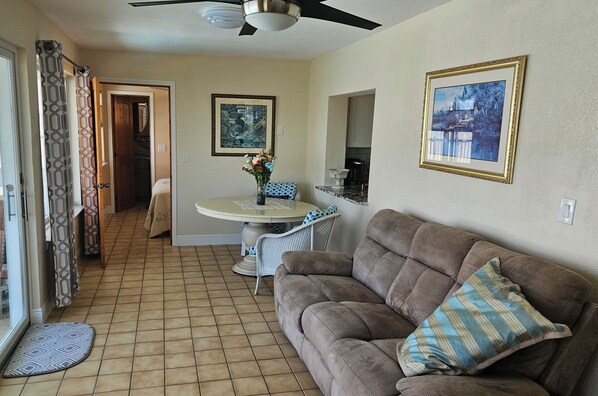 A living room with a brown sofa, a dining table with chairs, a ceiling fan, and a door leading to another room. - Canal-Front Gulf Coast Getaway (New Port Richey)