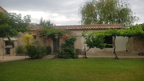 Un pati amb una paret de pedra, una pérgola amb flors vermelles i un prat verdós.