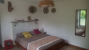 Un dormitori amb un llit, un mirall, una estant amb objectes decoratius i un ventilador de sostre.