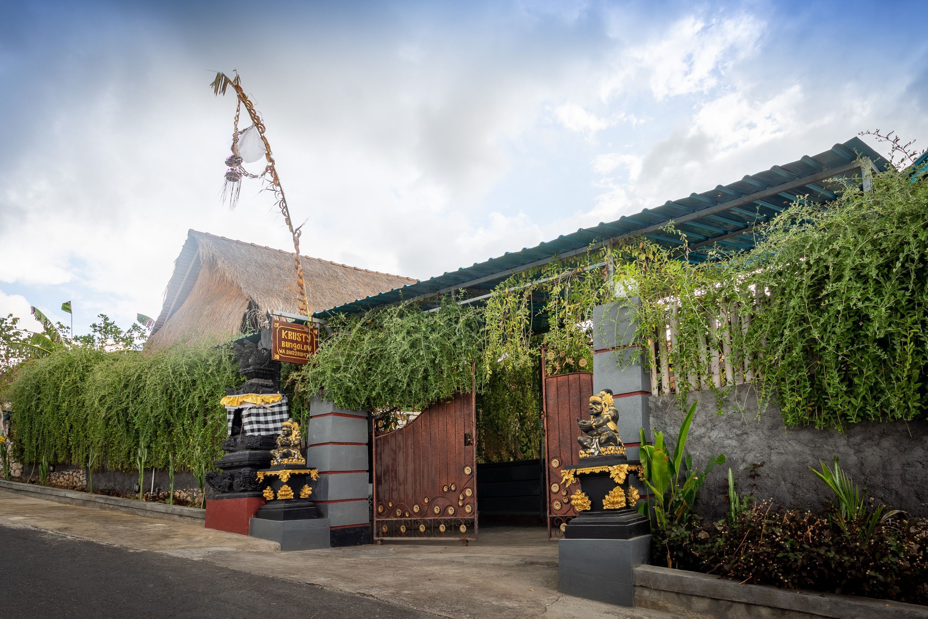 A traditional gate with intricate carvings and a signboard, leading to a building with a thatched roof.