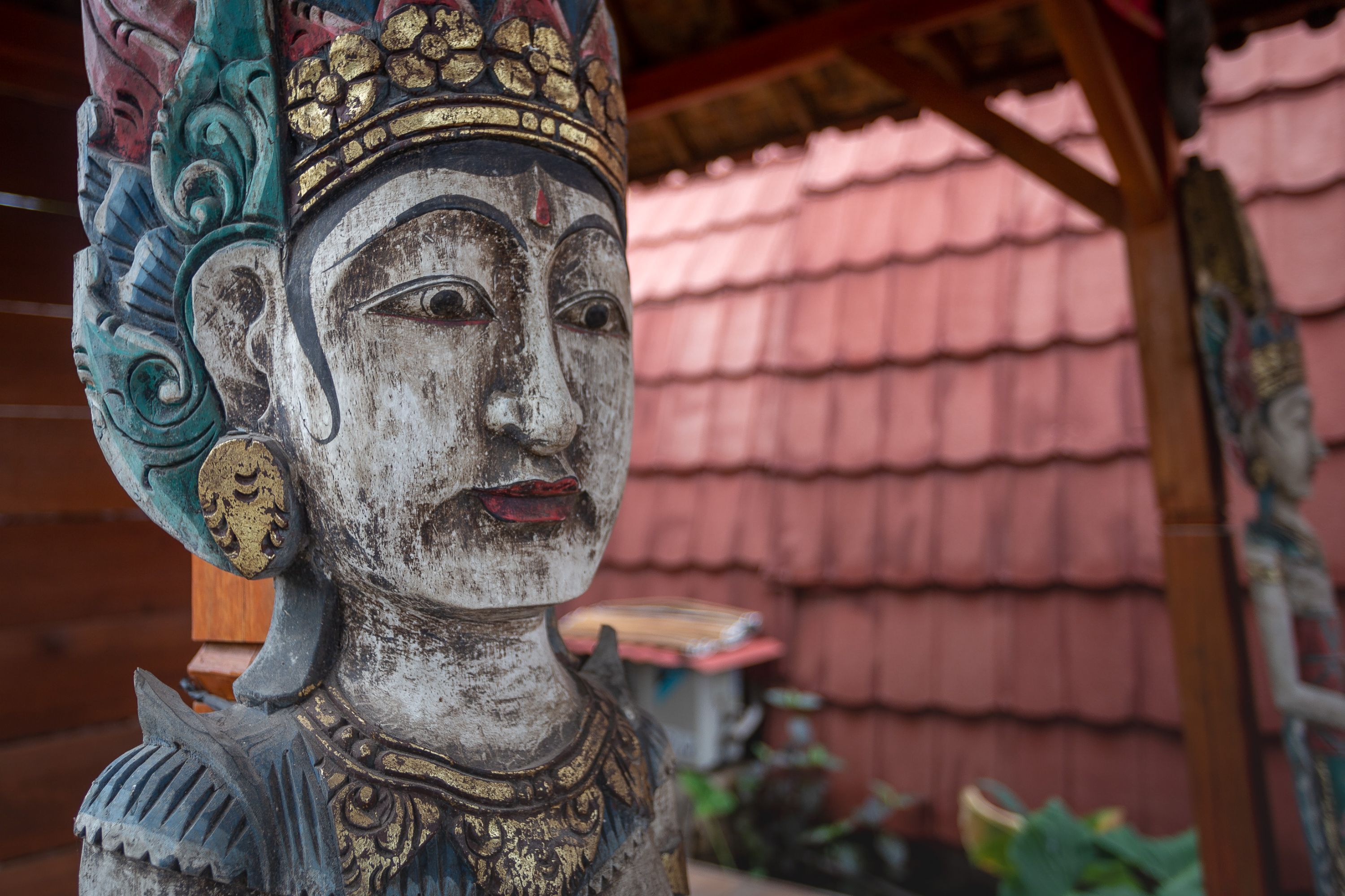 Una estatua con tallas intrincadas y una estructura de tejado tradicional al fondo.
