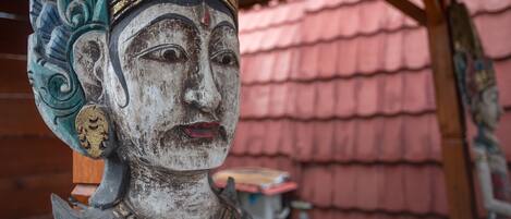 Una estatua con tallas intrincadas y una estructura de tejado tradicional al fondo.
