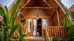 A wooden cabin with a pitched roof, a porch with wooden railings, and large green plants in the foreground. - Penida Krusty Hill (Penida Island)