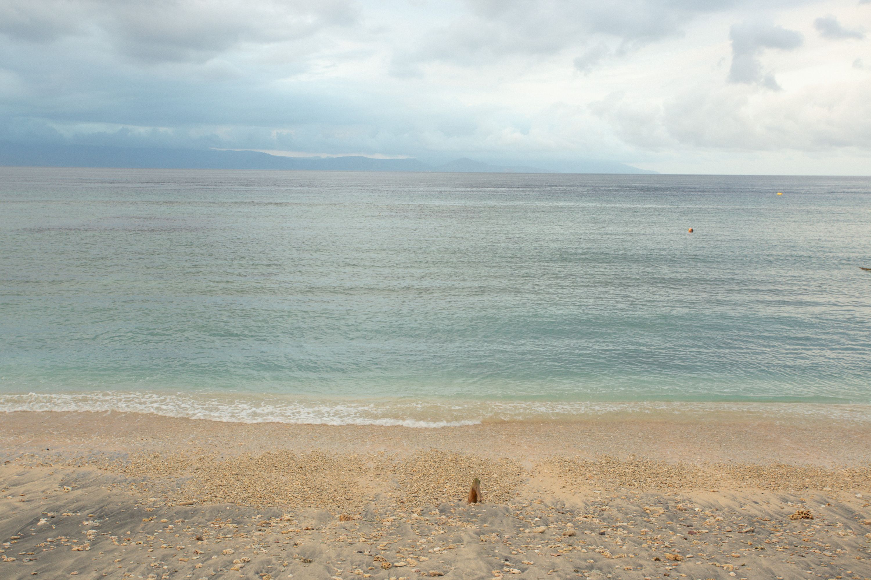 A beach with a sandy shore and calm sea under a cloudy sky.