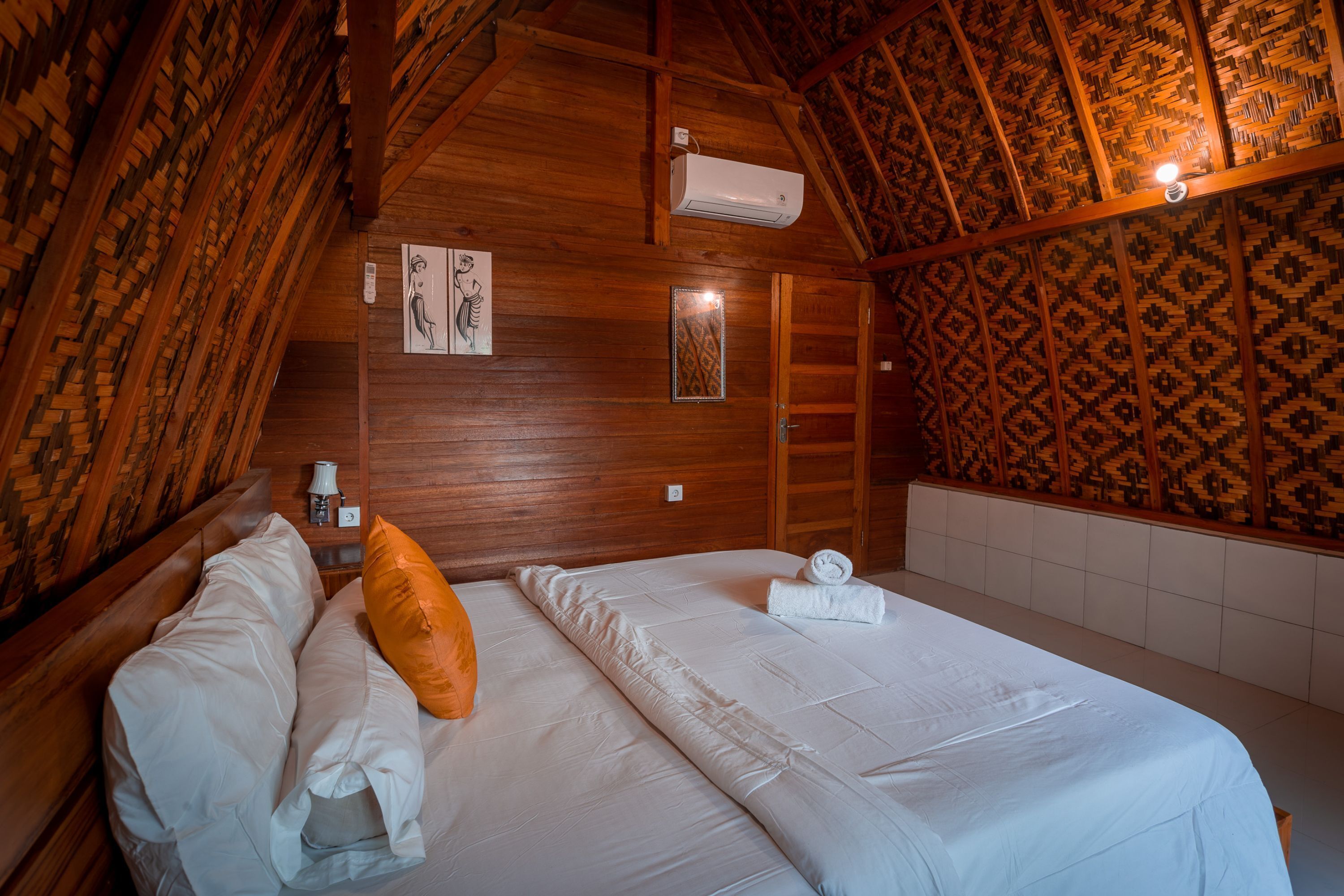 A wooden room with a bed, a wall-mounted air conditioner, and patterned wallpaper.