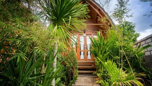 A wooden house with a thatched roof, surrounded by lush greenery and a stone wall. - Penida Krusty Hill (Penida Island)