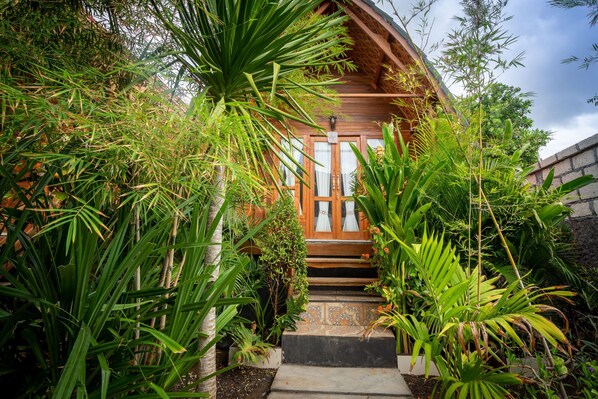 A wooden house with a thatched roof, surrounded by lush greenery and a stone wall. - Penida Krusty Hill (Penida Island)