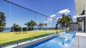 A swimming pool with a clear view of the ocean, surrounded by a well-maintained lawn and palm trees. - Lakes Hotel Serviced apartments (Toukley)