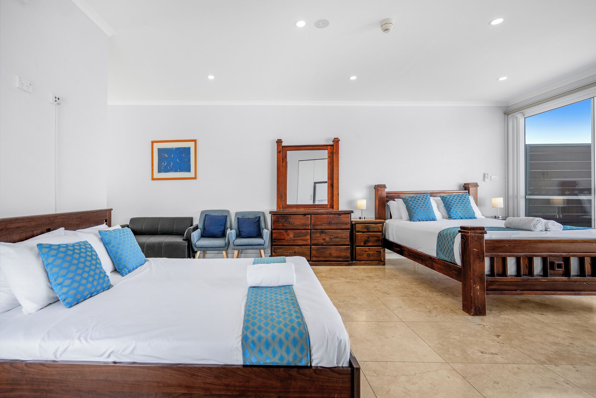 Habitación de hotel con dos camas, cómoda, espejo y ventana con vistas.