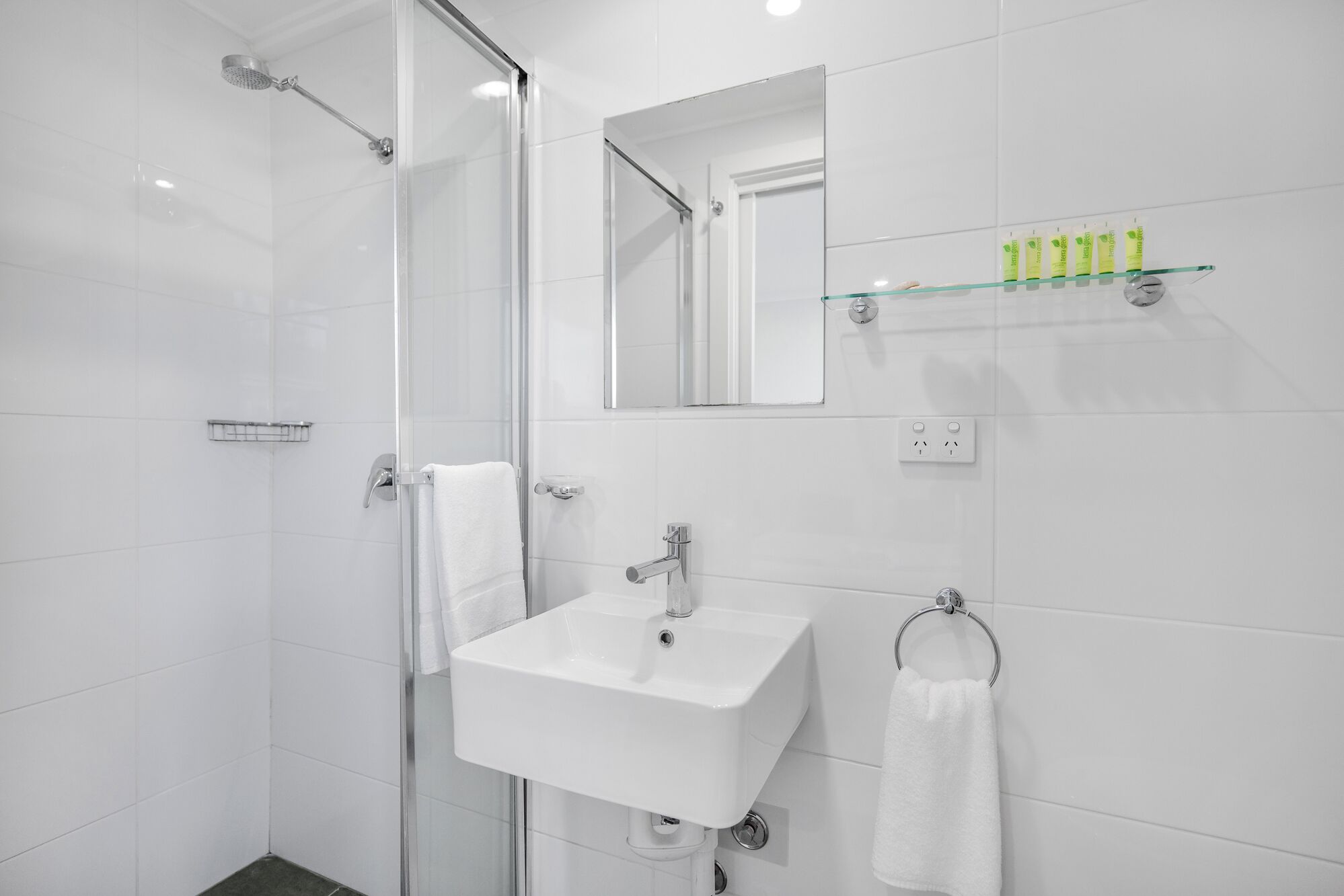 A modern bathroom with a glass shower enclosure, a white sink, and a mirror above it.