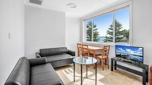 A modern living room with a sofa, a glass-top coffee table, and a TV. - Lakes Hotel Serviced apartments (Toukley)