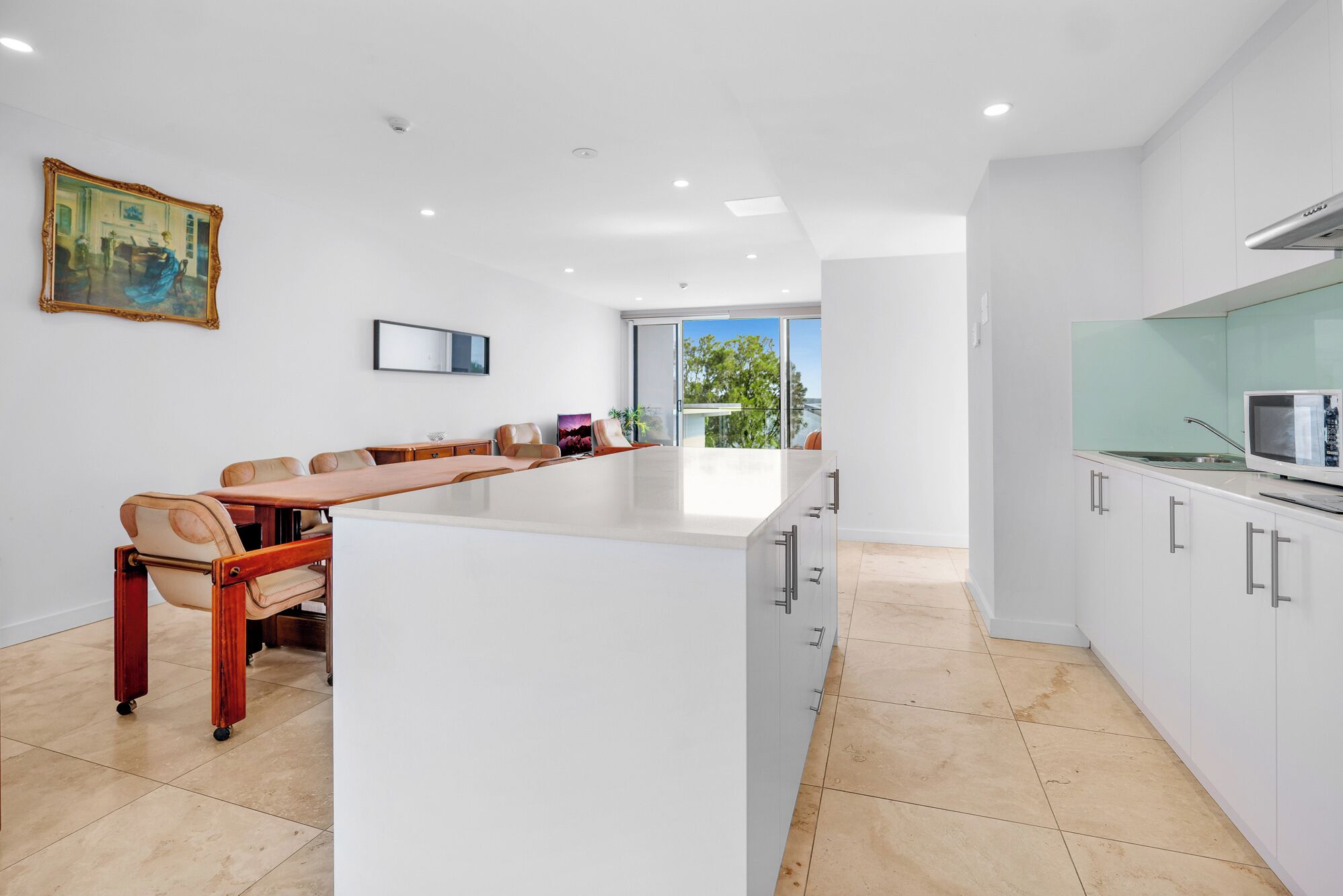 Una cocina moderna con una isla central, armarios blancos y un comedor con una mesa larga y sillas.