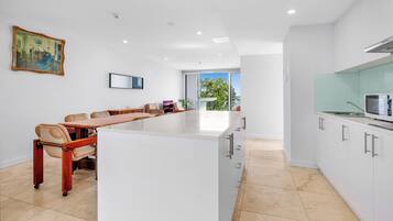 Una cocina moderna con una isla central, armarios blancos y un comedor con una mesa larga y sillas.