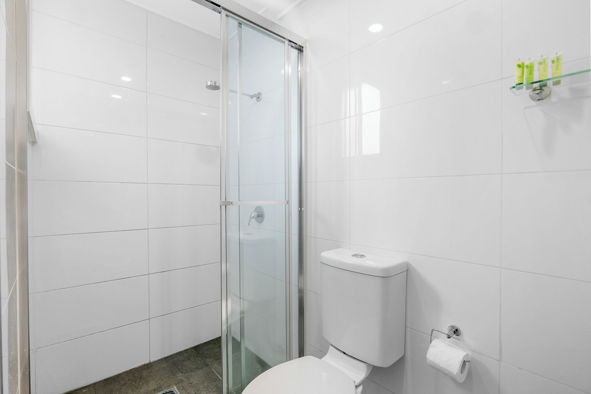 A modern bathroom with a glass shower enclosure, a white toilet, and a paper towel dispenser.