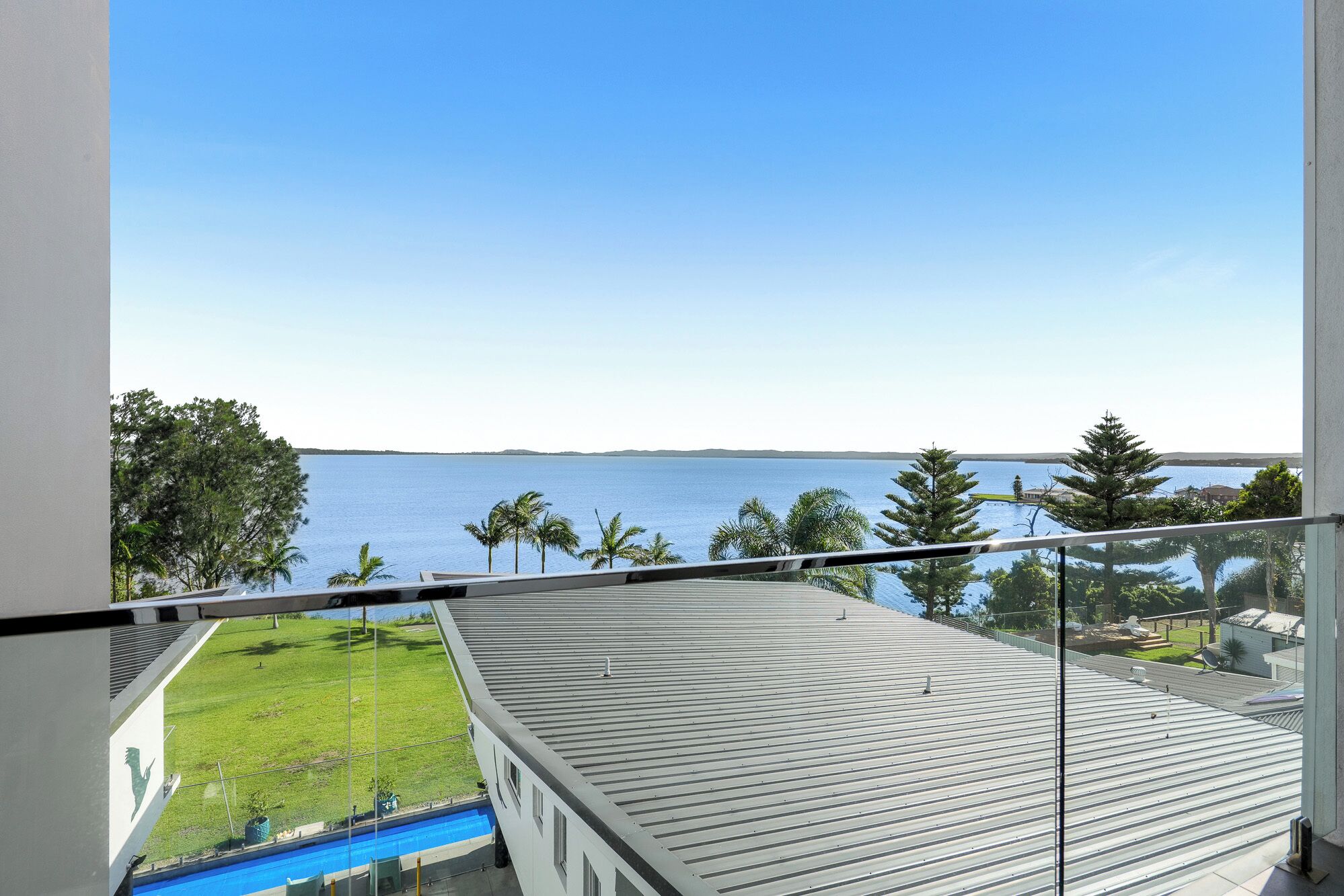 Ein Balkon mit Blick auf ein ruhiges Meer und eine begrünte Fläche mit Bäumen.