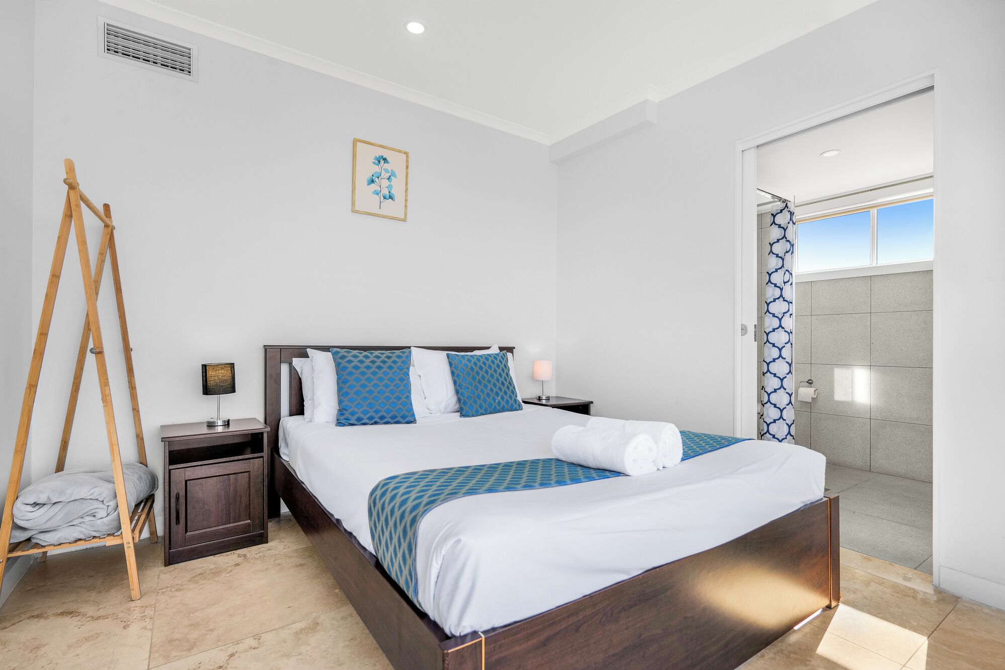 A neatly made bed with a wooden headboard, a bedside table with a lamp, and a wooden ladder leaning against the wall.