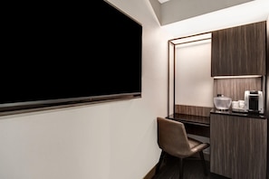 A hotel room with a large flat-screen TV, a wooden vanity with a mirror, a chair, and a coffee maker. - Springhill Suites Midtown Manhattan/park Avenue (New York)