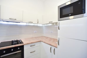 A kitchen with white cabinets, a built-in microwave, a stove, and a countertop. - Barbeta Accommodation (Budva)
