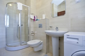 A modern bathroom with a glass shower enclosure, a toilet, a sink, and a washing machine. - Barbeta Accommodation (Budva)