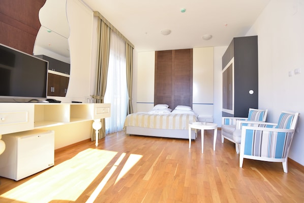 A modern hotel room with a bed, a TV, a desk, a chair, and a small fridge. - Barbeta Accommodation (Budva)