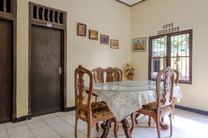A dining area with a glass-top table, floral tablecloth, and wooden chairs. - Spot On 1847 Hotel Maya (Beru)